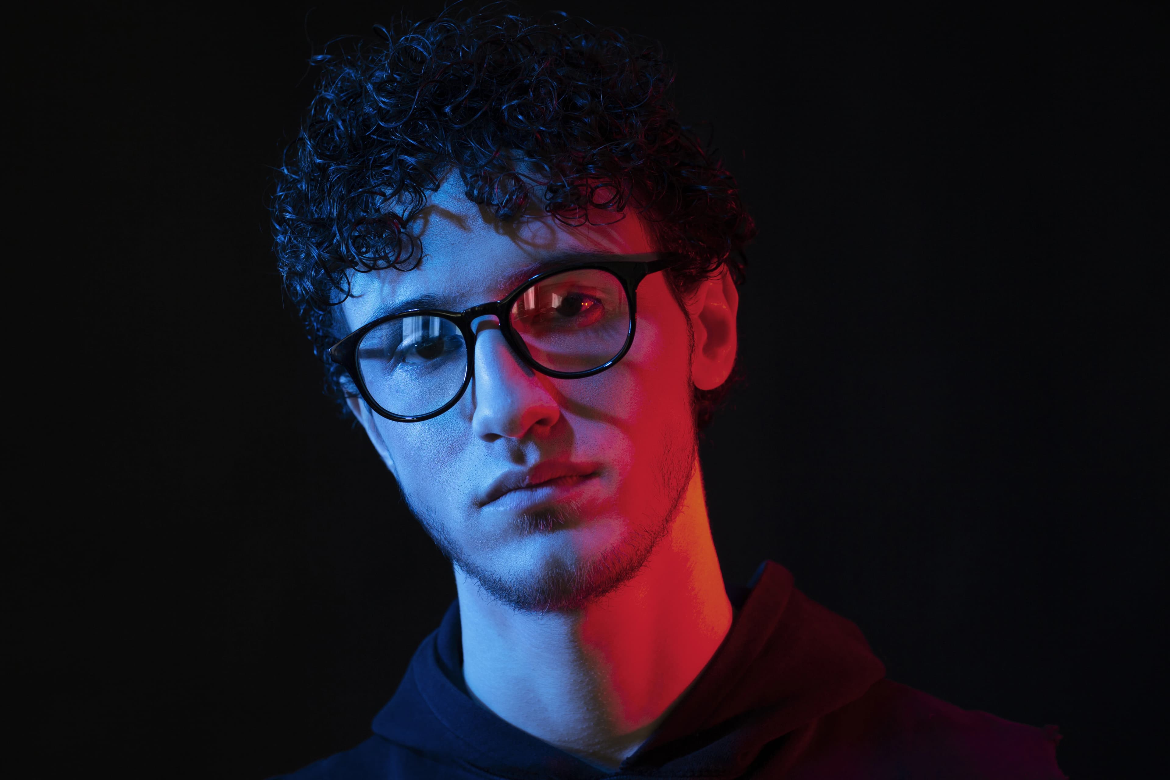 AI Headshot of man wearing glasses with curly hair in dramatic red and blue lighting, dark background studio portrait.